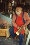 Man Carves Wooden Gnomes in Vendor's Tent by Richard Hoffman